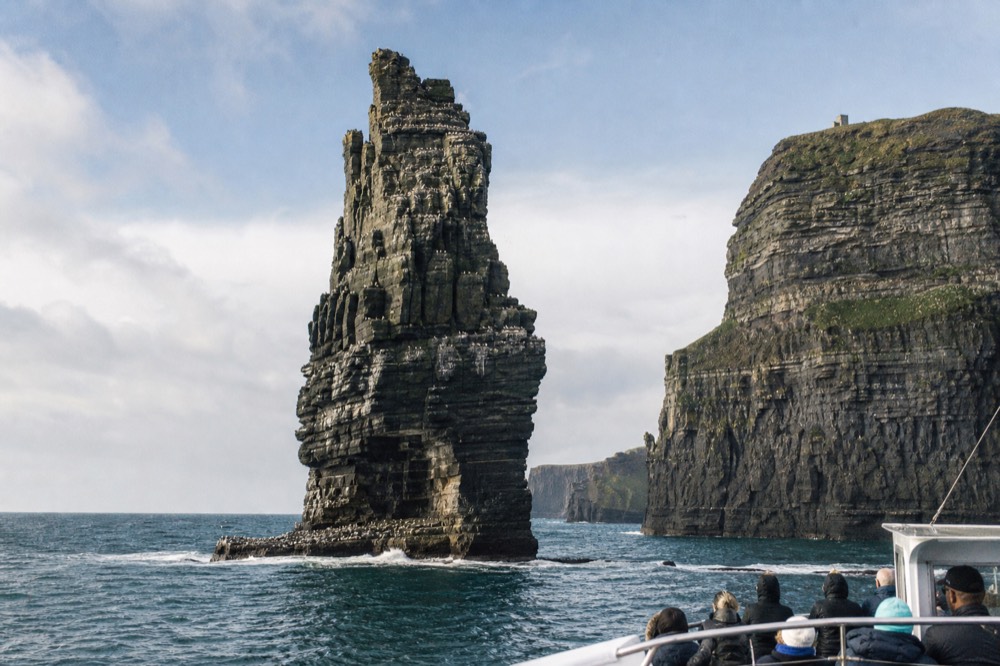 The An Branan Mor sea stack rising sheer from the Atlantic at the foot of the Cliffs of Moher, its ledges white with thousands of nesting seabirds, spray at its base.